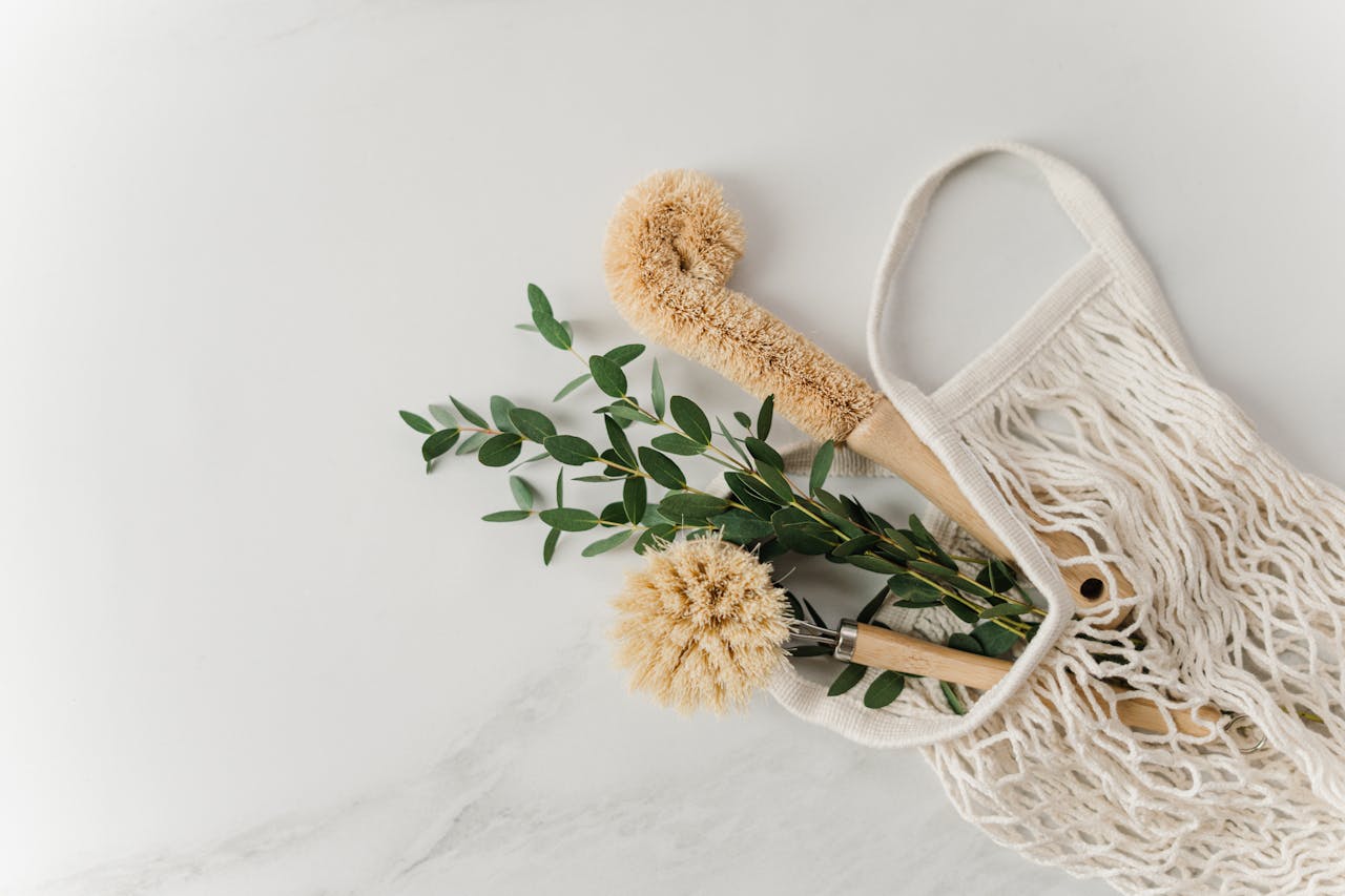 hero-img Eco-friendly cleaning brushes and eucalyptus branches in a reusable net bag on white surface.